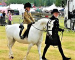 Junior girl riding a white pony with adult holding the reins